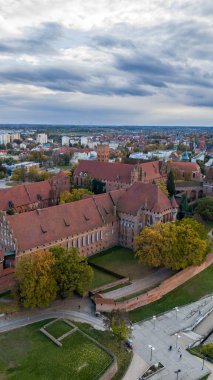 Hava aracı görüntüsü, Malbork Kalesi 'nin Polonya' nın Malbork şehrinde kuleleri, çentikli duvarları, kiremitli çatıları, avluları ve bulutlu ışık altında çimenlikleri olduğunu gösteriyor..