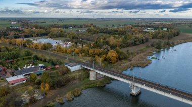 Polonya 'nın Malbork kenti yakınlarındaki Nogat Nehri' nin insansız hava aracı görüntüsü, modern bir yol köprüsü, yama alanları, sazlık körfezleri, küçük evler ve düz düzlükler üzerine yayılmış gün ışığı..