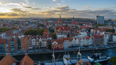 Gdansk Eski Kasabası 'nın hava görüntüsünde Motlawa Nehri, kanolar, rıhtımlar ve St Mary Kilisesi gibi kırmızı tuğlalı Gotik yapılar, sıcak altın ışık, çatılar ve caddeler görülüyor..