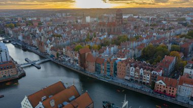 Hava görüntüsü Gdansk Eski Kasabası 'nın Motlawa Nehri kıyısında altın saat olduğunu gösteriyor. Aziz Meryem Kilisesi yükselir, Gdansk Turnası teknelerin yanında durur ve sıcak ışık yansıtır..