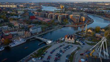 Polonya 'nın Gdansk kentinin hava görüntüsü Motlawa Nehri, Granary Adası, Gdansk Turnası, geniş bir yaya köprüsü, dönme dolap, tur botları ve sıcak ışık altında uzak tersane vinçlerini gösteriyor..