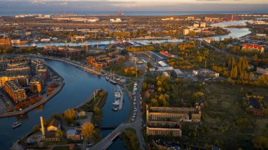 Polonya 'nın Gdansk kentinin havadan görünüşüne göre Motlawa Nehri, kanallar, tersaneler, marinalar ve sıcak altın ışıklı kırmızı çatılar, vinçler, parklar, bataklıklar ve uzak liman.