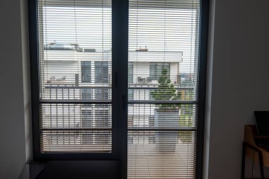 Zeminden tavana yatay perdeli cam kapı Gdansk 'ta küçük bir balkona bakıyor, metal korkuluklar, uzun saksılar ve gün ışığında beyaz apartman blokları..