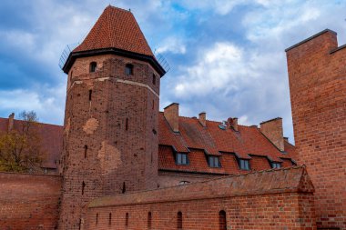 Kırmızı tuğlalı Gotik kule ve kuzey Polonya 'daki Malbork Kalesi' nin çentikli duvarları, sarp kırmızı kiremitli çatılar ve bulutlu ışık altında ok yarıkları, ortaçağ dayanıklılığını taşıyor..