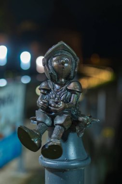 Bronz bir cüce şövalye, elleri bağlı bir direkte oturuyor. Polonya 'daki Malbork Kalesi' nin yakınlarında. Bokeh ışıklarının arkası bulanık..