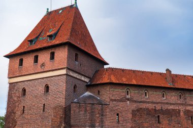 Malbork Şatosu 'nun yakınında, Polonya' da kırmızı tuğlalı bir kule, duvarlar, terracotta çatıları, yatakhaneleri, ok yarıkları ve mızrak açıkları ve yumuşak gün ışığında yeşil budanmış saçaklar var..