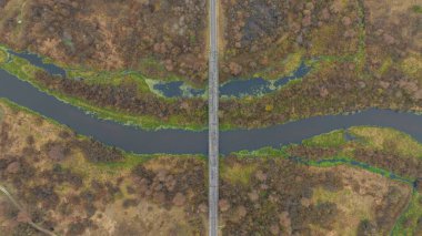 Hava manzarası, Belarus 'ta bataklık sulak alanları, alçak ormanlar, tarlalar, ağaçlıklar ve hatta yumuşak ışıklarla dolambaçlı bir nehri geçen dar bir köprü ve düz bir yol gösteriyor..