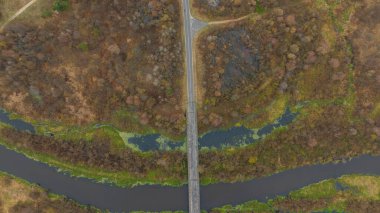 Havadan bakıldığında, Belarus kışındaki S eğrisi karanlık bir nehri geçen dar bir köprü ve düz bir yol görünüyor. Dalgalı sulak alanlar, yapraksız ormanlar ve sessiz kumral ve griler..