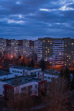 Minsk 'teki alacakaranlık, Sovyet döneminin sıcak pencereli panel bloklarını gösteriyor. Alçak kırmızı ve beyaz binalar, sokak lambaları turuncu havuzları dökerken çıplak ağaçların arasında oturuyorlar..