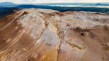 İzlanda 'daki Myvatn Gölü yakınlarındaki Namafjall Hver' in hava görüntüsünde sülfür menfezleri, mineral kabukları, pastel rengi ve pas bantları, koyu lav ve bulutlu ışık altındaki bir çatlak görülüyor..