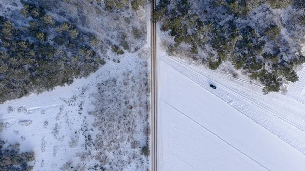 Polonya 'nın Nowy Lubiel kentinin hava görüntüsü ormanı ve tarlaları ikiye bölen bir kar yolu gösteriyor. Karanlık bir araç doğru yolda ilerliyor. Serin gün ışığı ve berrak gölgeler düzeni tanımlar.
