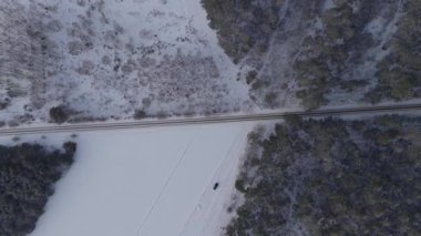 Nowy Lubiel yakınlarındaki havadan bakıldığında düz bir demiryolu, tarla sürülmüş bir tarla ve çam ağacı ormanı görülüyor. Kışın karlı bir yolda giden karanlık bir araç..