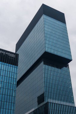 Polonya 'nın Katowice şehrinde üst üste yığılmış hacimli ve kantilli cam gökdelen. Yansıtıcı perde duvarları ve koyu mulyonlar bulutlu bahar gökyüzünün altında duruyor..