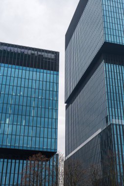 Polonya 'nın Katowice şehrinde iki cam ve çelik ofis kulesi yükseliyor, orta kısmı kaplanmış, üst bandı dinlenmiş ve sokak perspektifinden çıplak ağaçlarla çevrili..