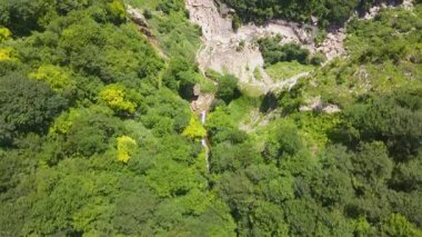 Hava manzarası, Gürcistan 'ın Yukarı Svaneti şehrinde dik bir kayalık vadi ve dar bir şelale gösteriyor. Yeşil çatı binaları, çitli yollar ve platformlar şelalenin üzerinde oturur..