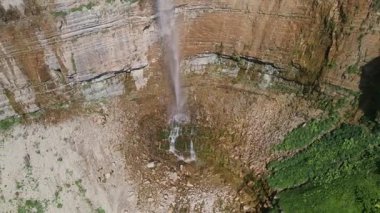 Hava aracı görüntüsü Yukarı Svaneti 'deki bantlı kireçtaşı uçurumunda dar bir şelale olduğunu gösteriyor. Parlak yaz güneşi, sis sütunu, basamaklar, kayalık talus kasesi..