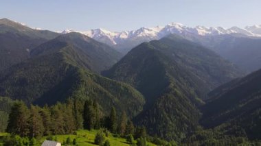 Svaneti, Gürcistan 'ın hava manzarasında orman tepeleri, bir Svan kulesi, bir taş çoban kulübesi, alp çayırları, derin vadiler ve açık gökyüzü altında karlı Büyük Kafkaslar görülüyor..
