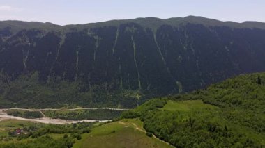 Gürcistan 'ın Yukarı Svaneti kentindeki bir dağlık vadide teraslı otlaklar, kümelenmiş köyler, örülmüş bir nehir, dolambaçlı bir yol ve açık yaz ışığı altında Shkhara' nın bulunduğu bir hava tavası..