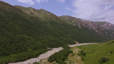 Gürcistan 'ın Svaneti kentindeki hava sahasında solgun bir nehir yatağı, sık bir orman, kayalık tepeler, çimenli teraslar ve dengeli bir dron taraması sırasında sel ovası görülüyor..