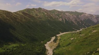 Gürcistan 'daki dik bir Svaneti Vadisi' ndeki hava aracı örülmüş kayalık bir nehir yatağı, karanlık bir orman, çimenli dağlık yamaçlar, kırlangıçlar ve ılık gün ışığı altında karlı tepecikler gösteriyor..