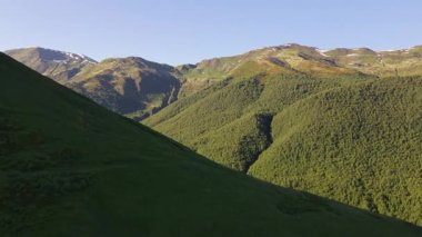 Gürcistan 'ın Svaneti kentindeki kayan tepeler ve alp çayırlarının havadan görünüşü. Kamera ileri ve aşağı doğru kayıyor, bahar sonu kar şeritleri ve V şeklinde vadiler görülebilir..