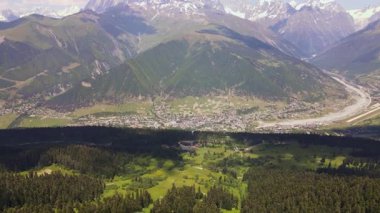 Küçük pist, örülmüş nehir, kozalaklı ormanlar, alp çayırları ve parlak yaz ışığında beyaz tepeli Kafkasya 'nın hava aracı görüntüsü..