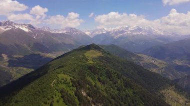 Gökyüzü kamerası Gürcistan 'ın Svaneti kentindeki çimenli bir tepe boyunca süzülerek, bulutlar vadilerin üzerinden geçerken ve Büyük Kafkaslar açık gün ışığında zirveye çıkarken barakaları ve köyleri geçiyor..