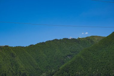 Gürcistan 'ın batısındaki ormanlık tepelerin gün ortası manzarası, küçük beyaz gözlemevi kubbeleri uzak bir sırt noktası, parlak ışık, geniş kompozisyon, ince bir kablo mevcut..