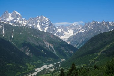 Svaneti, Georgia vadisi Ushba ve Tetnuldi kulelerine doğru uzanıyor. Merkezi bir sirk buzulu, açık bir yaz gökyüzünün altında kozalaklı ve dağlık çayırların arasında örülmüş bir nehri besler..