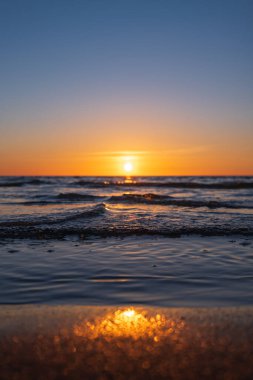 Baltık Denizi 'nin alçak açılı dalgaları Litvanya' da gün batımında kumlu kıyıları turluyor. Güneş ufukta süzülür, ıslak sahil altını yansıtır, dalgalar taze kalır, bokeh kum parlar..