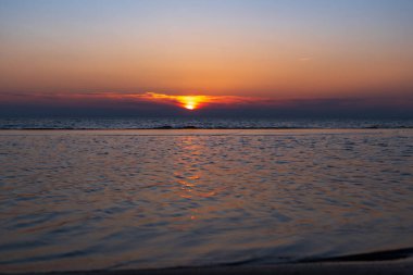 Akşamın geç saatlerinde güneş, Litvanya yakınlarındaki Baltık Denizi 'nde batar. Düz ufuk çizgisi, yumuşak sörf, soluk bir iz, dalgalanan su ve ipeksi uzun pozlama yansımaları vardır..