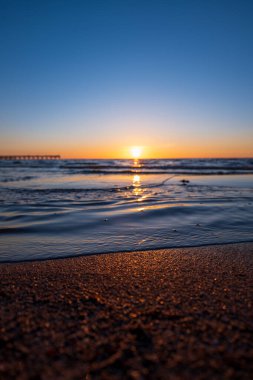 Alacakaranlık sahnesi gün batımında Baltık Denizi 'ni gösteriyor. Dalgalı su ve ıslak kum parıldıyor. Sol ufukta Palanga ya da Klaipeda yakınlarında uzun bir iskele var..