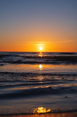 Alçak açılı günbatımı, Litvanya yakınlarındaki sakin dalgalara altın yansıyor. Portakaldan mavi gökyüzüne ince bulutlar ışığı yumuşatır, alacakaranlıktaki alacakaranlık gibi yansıtır..