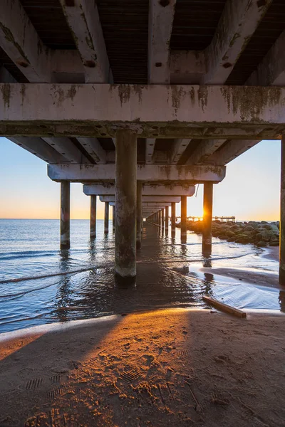 Yıpranmış beton iskele altındaki alçak açı, Baltık Denizi, Litvanya 'ya giden alg işaretli sütunları gösteriyor..