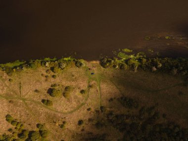 Litvanya 'daki hava manzarası, dar bir yolun sazlıklar ve karışık ağaçlarla çevrili karanlık ve yavaş bir nehirle buluştuğu nehir kenarındaki açıklığı gösteriyor..