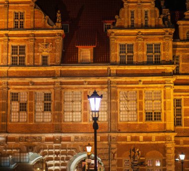 Sıcak ışık Gdansk 'ta Rönesans tuğlası cephesini yıkıyor. Antika bir sokak lambası parlak beyaz, uzun pencereler ve yontulmuş gablalar kemerli bir geçidi çerçeveler..