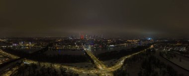Aerial winter night view of Warsaw shows the Vistula River, Swietokrzyski Bridge lit at center, the red Palace of Culture and Science, and Old Town lights by the banks.