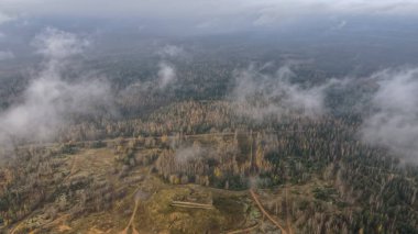 Hava görüntüsü, Dretunsky 'nin Belarus' ta sonbahar huş ve çam ağaçları, kumlu izler ve alçak bulutlar ve sis gibi merkezi beton bir sığınak ile eğitim alanının yukarıda sürüklendiğini gösteriyor..