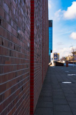 Yayalar kışın sokak seviyesinde çekilen heykel, su birikintileri ve modern cam yükseltileriyle yürürken uzun bir tuğla duvar rıhtıma çıkar..