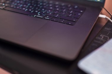 Polonya 'da bir masada ışıklı komut, opsiyon anahtarı ve pist takımına sahip şık bir dizüstü bilgisayar klavyesi bulunuyor. Beyaz şarj kablosu, bulanık bir telefon ve yanında metrik bir cetvel ile fişe takılır..