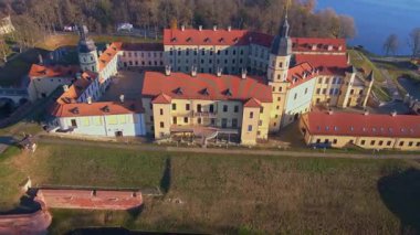 Beyaz Rusya 'daki Nesvizh Kalesi' nin hava aracı görüntüsü kırmızı çatılar, köşe kuleler, hendek, göl, sonbaharda park gösteriyor. Kamera geri çekiliyor ve öğleden sonra tepemizde süzülüyor..
