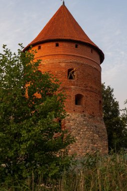 Yuvarlak kırmızı tuğla kule dik konik kiremit çatısı yükseliyor Litvanya 'da sazlıklar ve ağaçlar üzerinde, ok yarığı pencereler ve sıcak akşam ışığında kiriş.