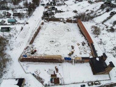 Hava görüntüsü, Belarus 'ta yenilenen, iskelesi, ağır ekipmanı, kerestesi, kırmızı çatılı galerisi ve kırsal bir köyün ortasında köşe kuleleri olan karla kaplı bir kaleyi gösteriyor..
