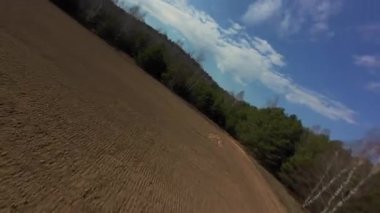 Dinamik hava görüntüleri yeşil ormanlarla çevrili yeni sürülmüş kahverengi tarla üzerinde seyahat ediyor. Çekim, açık gökyüzünün altında doğal ağaç sınırı ve ekilmiş tarım arazisi ile kırsal araziyi yakalar....