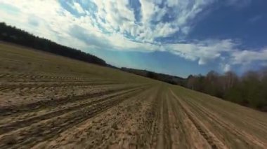 Yoğun ormanlarla çevrili geniş tarım alanlarında seyahat eden bir araçtan alınan dinamik hareket görüntüleri. Üzerinde beyaz bulutlar olan açık mavi gökyüzü huzurlu bir kırsal atmosfer yaratır....