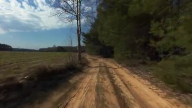 Tarımsal tarlalar ve çam ormanlarıyla çevrili düz toprak yol boyunca sürüş görüntüleri. Dağınık bulutlu açık mavi gökyüzü sakin bir kırsal atmosfer yaratır....
