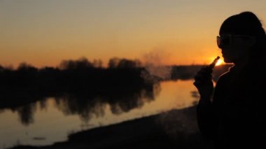 kadın günbatımında elektronik sigara içiyor