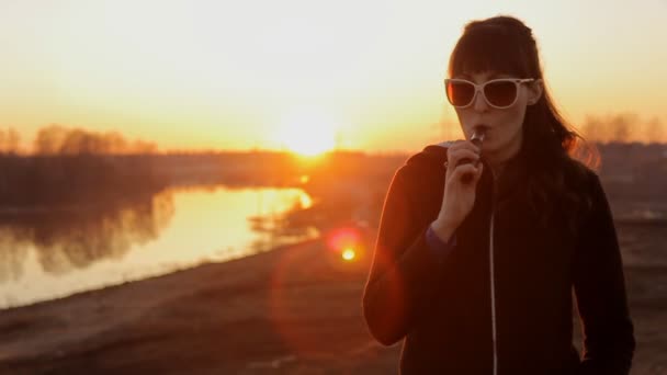 Girl in sunglasses at sunset smoking electronic cigarette — Stock Video