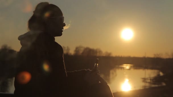 Mulher fuma um cigarro eletrônico ao pôr do sol — Vídeo de Stock