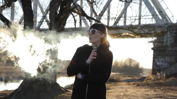 Chica en el fondo del puente fuma un cigarrillo electrónico, muñeca — Vídeo de stock